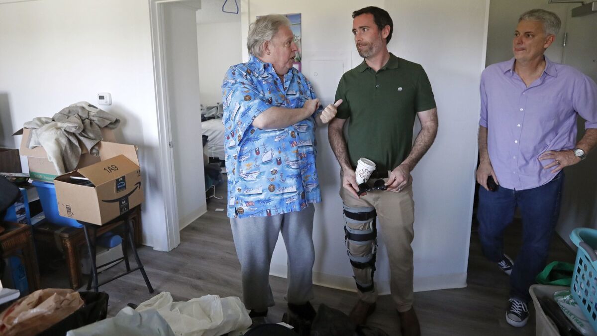 Navy veteran Glen Lipton, 67, left, talks to Kyle Paine, president of Community Development Partners, center, and Larry Haynes, executive director of Mercy House, in his unit at the Cove Apartments in Newport Beach.