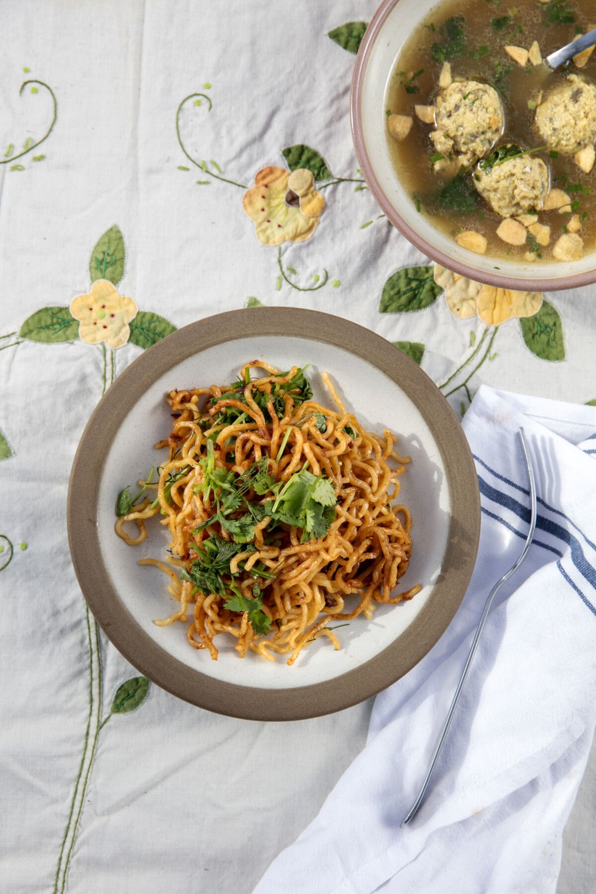 A plate of noodles, seen from overhead, next to a bowl of fish balls in fish broth