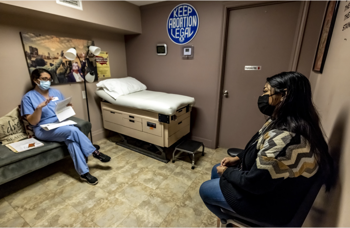 A healthcare provider speaks with a patient in an exam room.