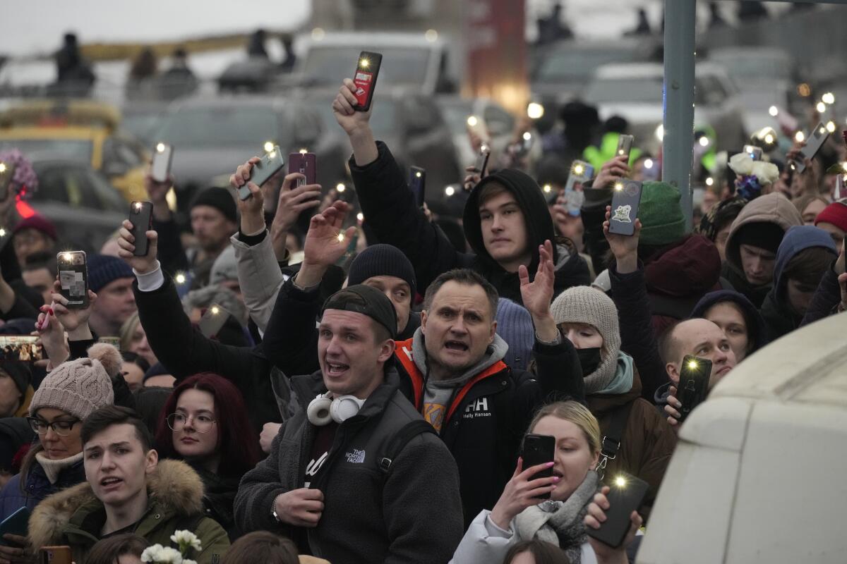 A crowd of people gather on a street, many holding up lights from their cellphones