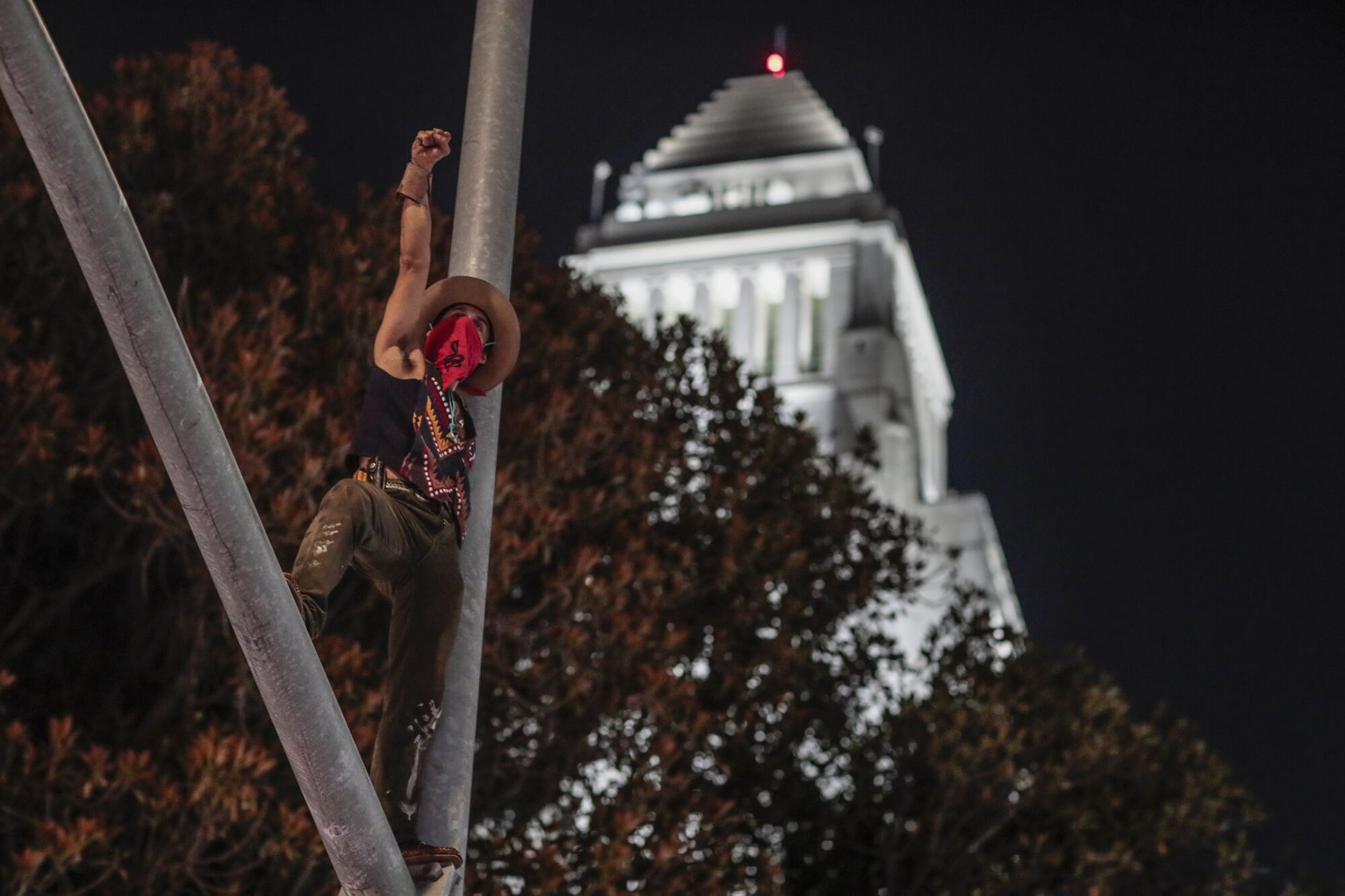 A lone demonstrator climbs a light pole at the corner of Main and 1st Street in downtown Los Angeles.