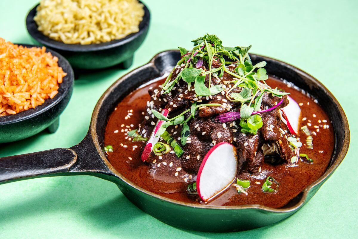 Mission Fig Mole served in a black pan, beside two black bowls full of rice.