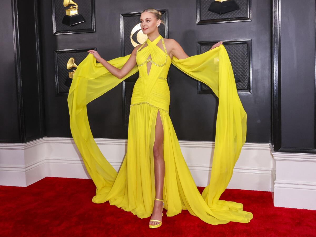 A woman in a draped yellow gown poses on a red carpet