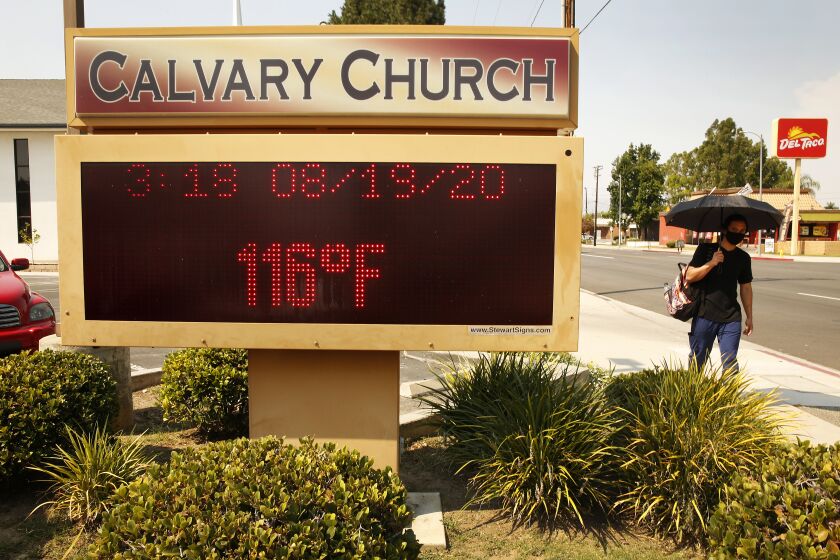 WOODLAND HILLS, CA - AUGUST 19: Leo Dumayag with umbrella for shade walks past the thermometer at Calvary Church in Woodland Hills as it registers 116 degree's Fahrenheit Wednesday afternoon as the Southland's fiercest heat wave entered its second week threatening "excessive heat" and elevated fire danger. Los Angeles on Wednesday, Aug. 19, 2020 in Woodland Hills, CA. (Al Seib / Los Angeles Times