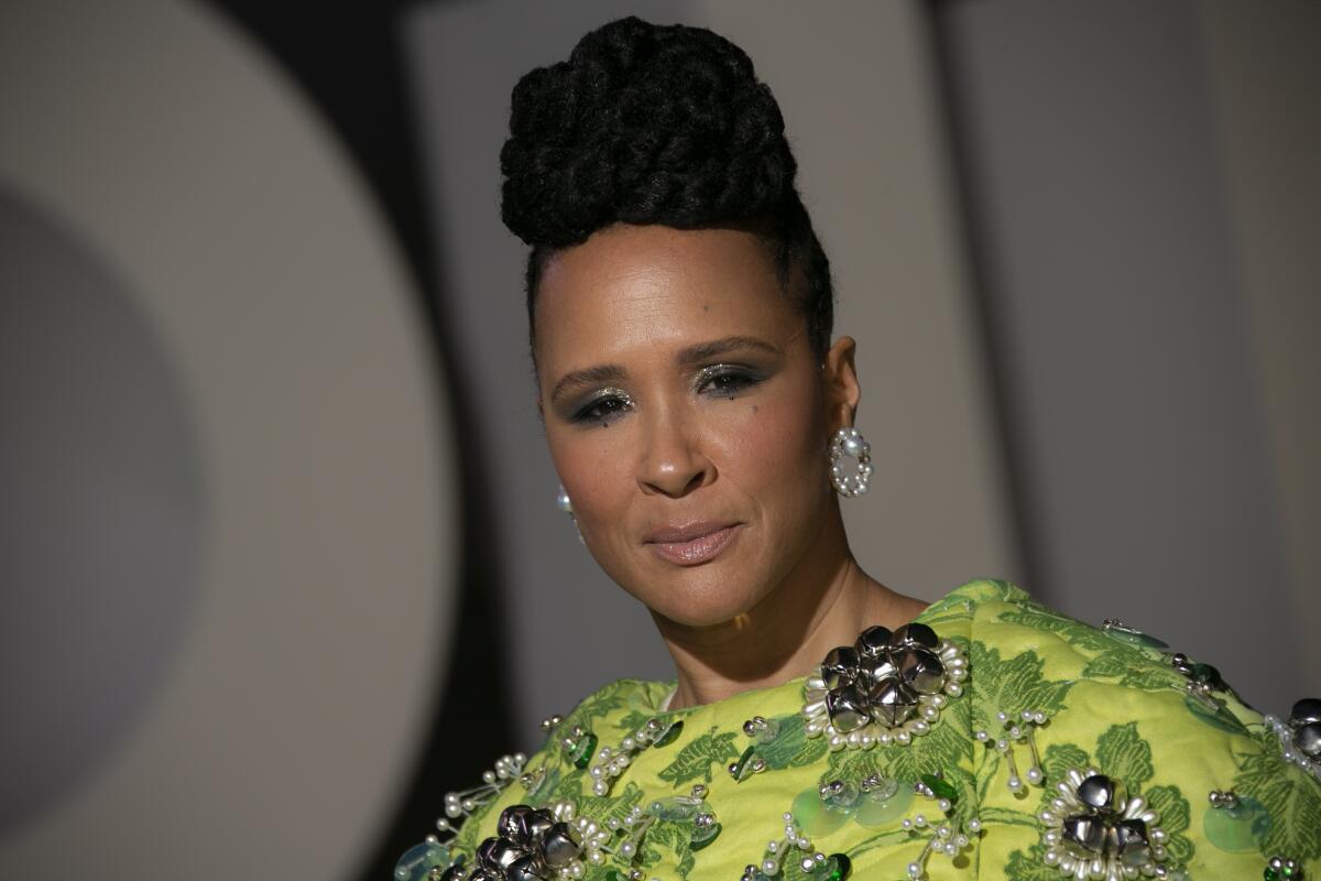 A woman in a green dress and upswept hairdo poses for photographers