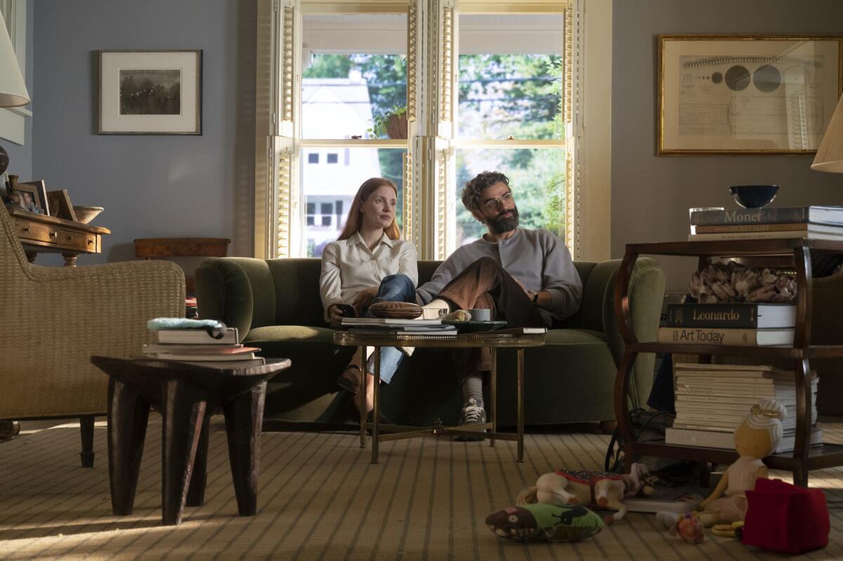 A man and a woman sit on a couch in a living room.