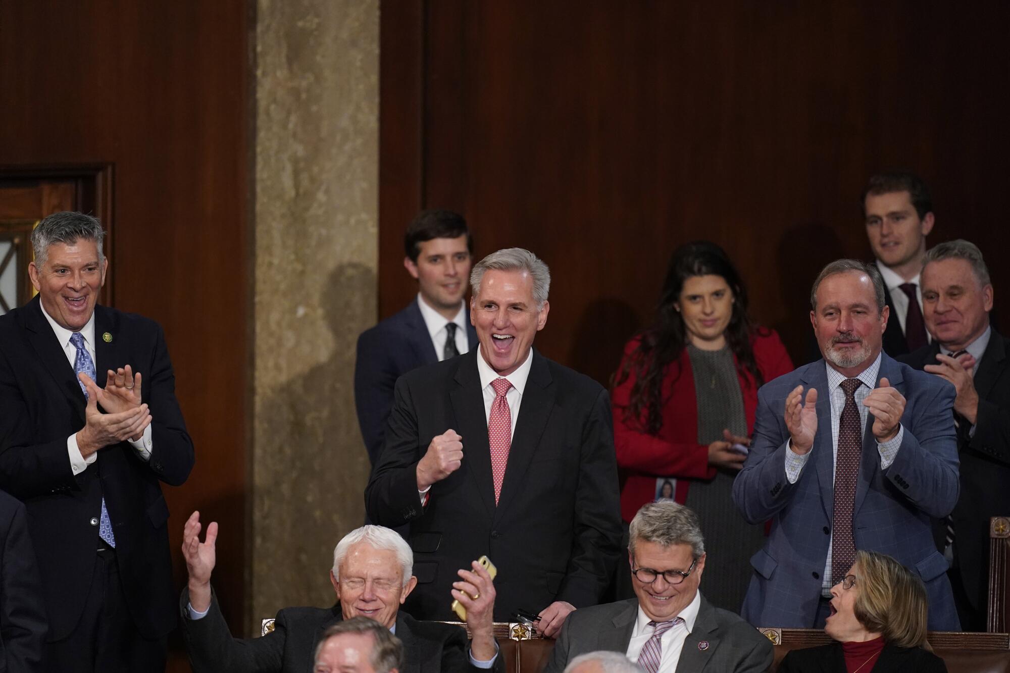 A man in a suit pumps his fist as others around him clap.