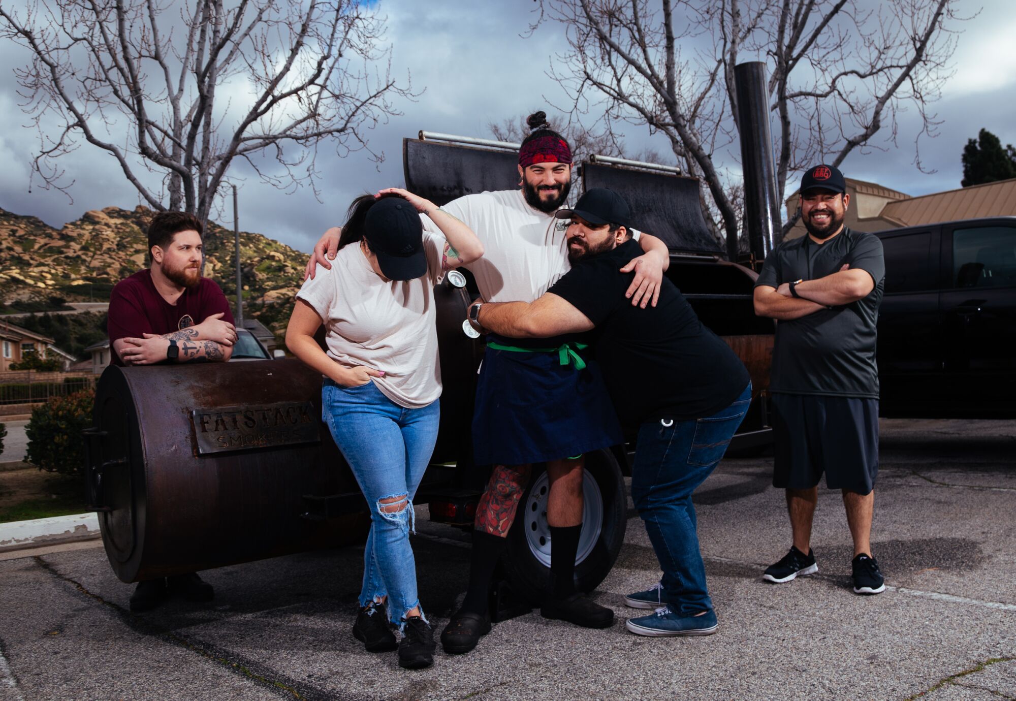 Zef BBQ owners and workers smile and hug around a smoker.