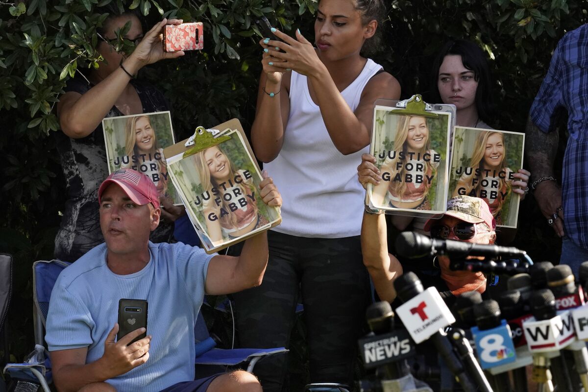 People hold up photos of Gabby Petito in front of news microphones