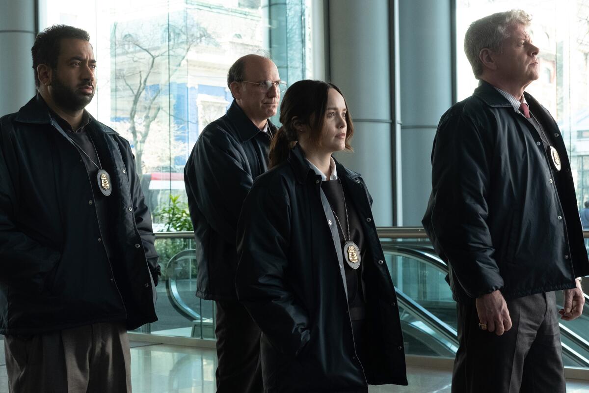 Four people with FBI badges and dark jackets stand in a glass-walled building.