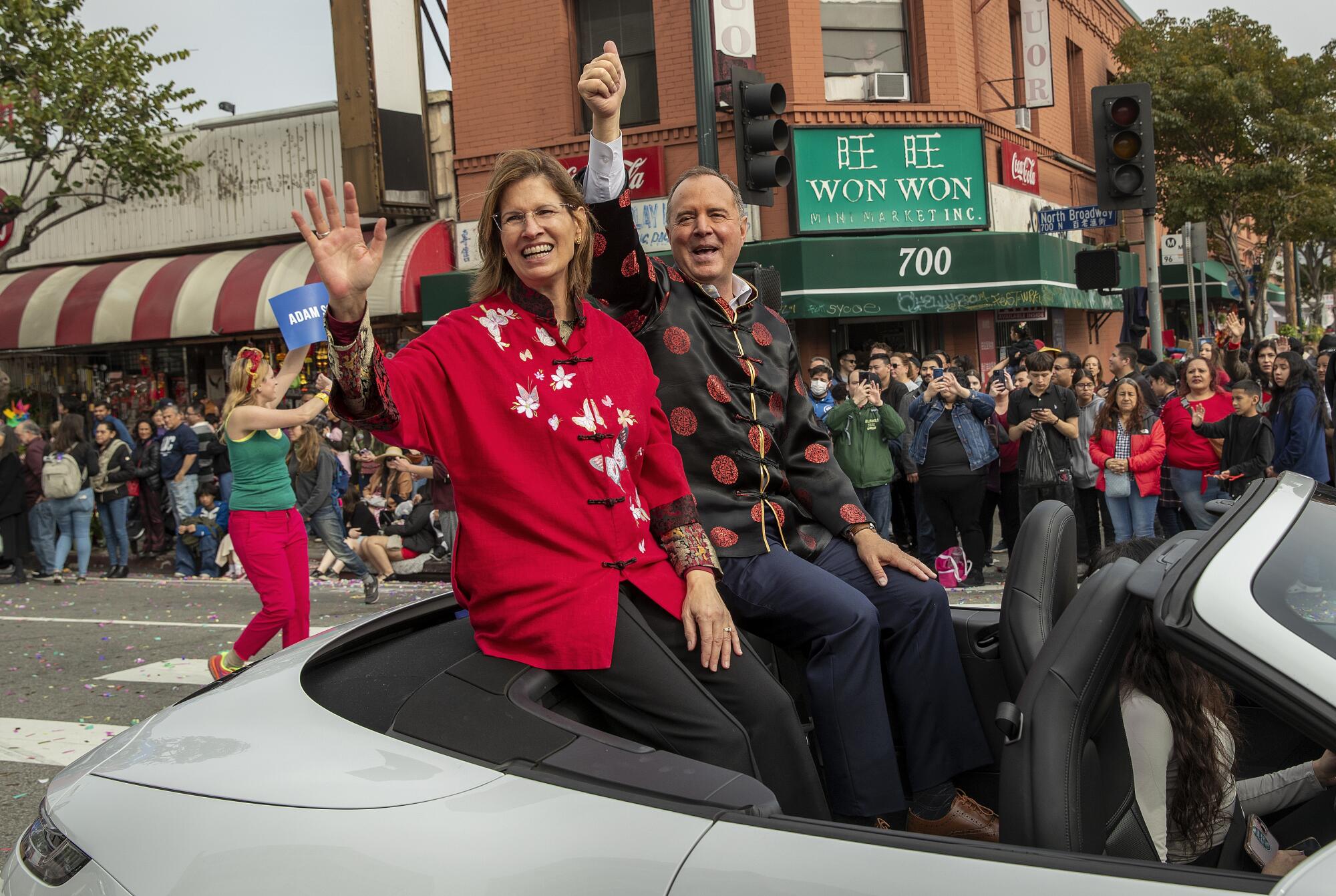 Adam Schiff and wife Eve, in traditional Chinese garments, wave from a convertible as a crowd lines the street behind them