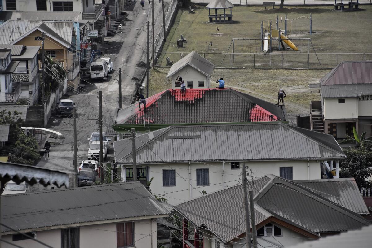 People clean volcanic ash from the red roof of a home.