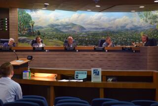 five people sit at a brick and wooden city council dias with a mural of mountains behind them