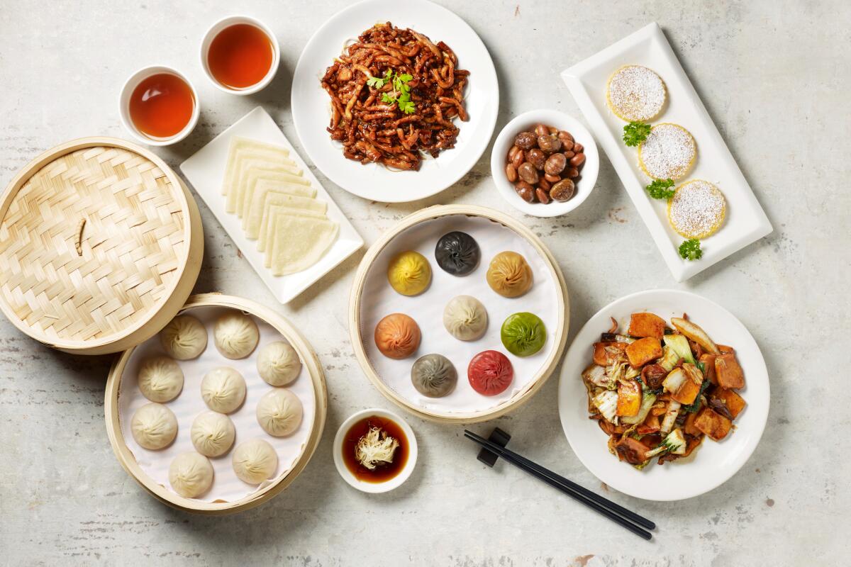 Round woven steamer baskets open to display dumplings of different colors, as well as other dishes.