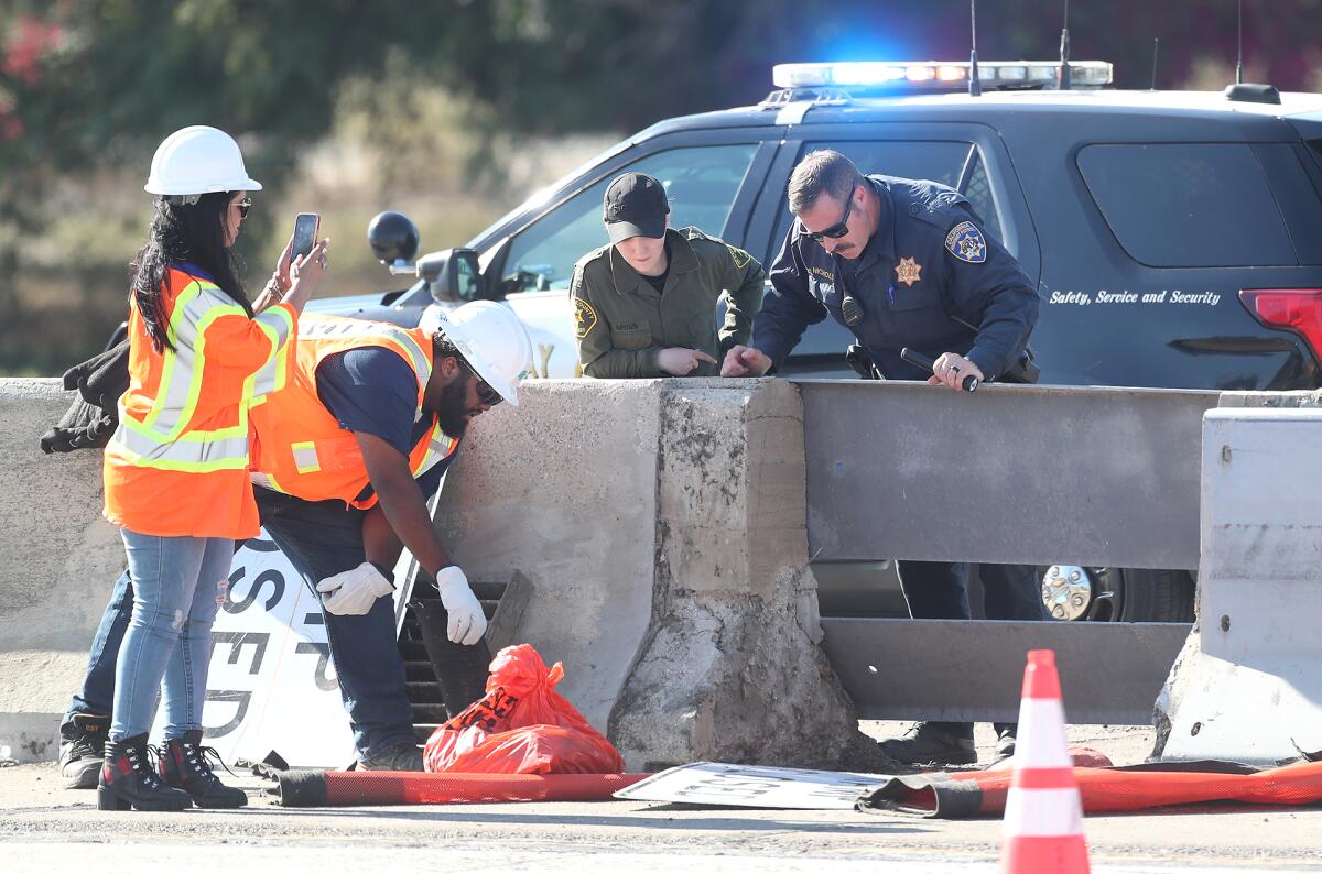 Law enforcement officers in uniform and transportation workers in high-visibility vests around a drainpipe near a freeway.