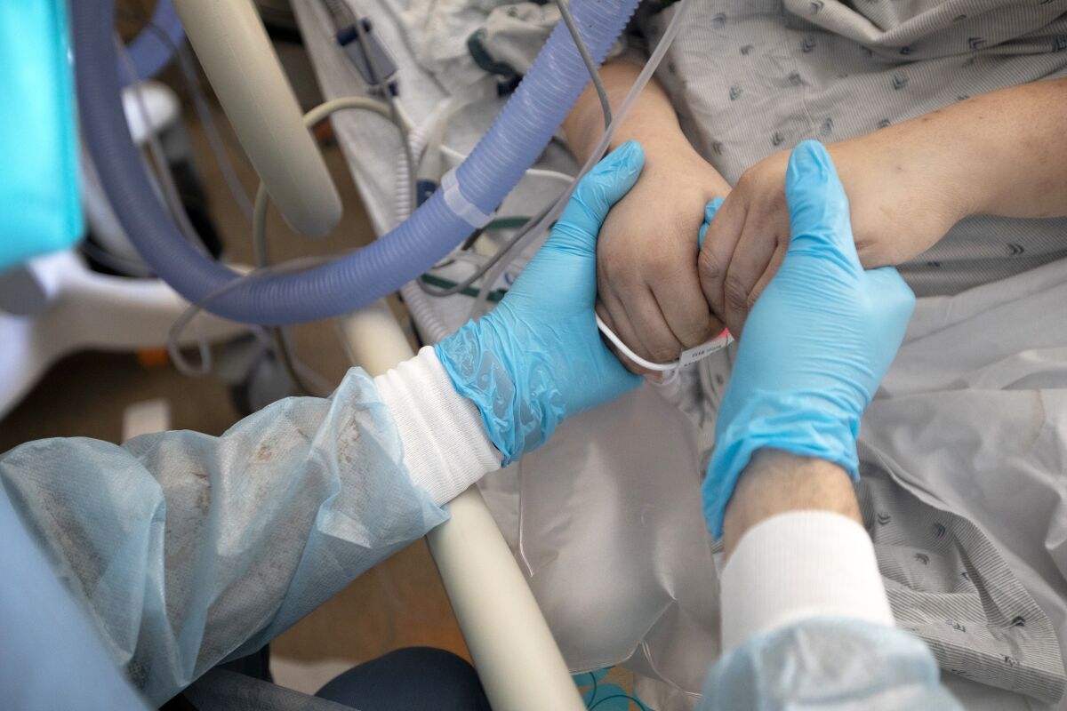 A gloved hospital worker holds a patient's hands.