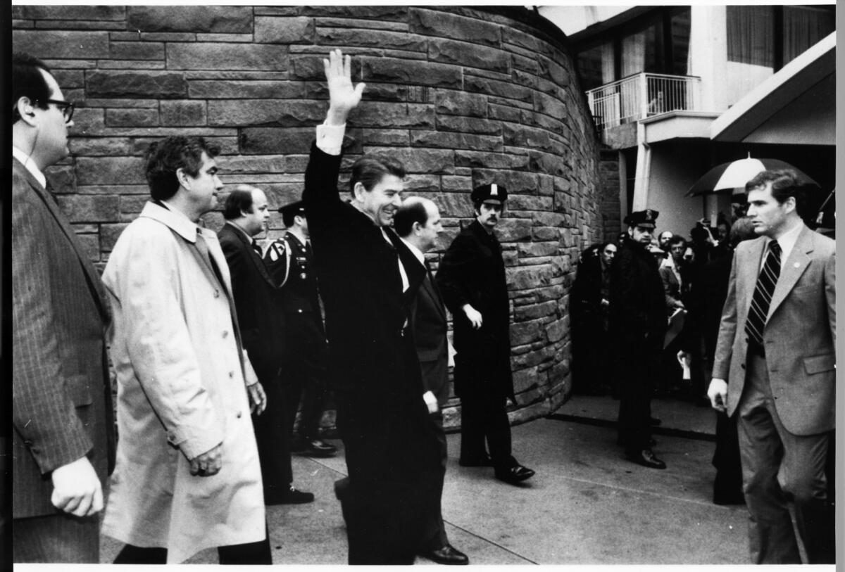 President Reagan waves just before being shot outside a Washington hotel in 1981. Secret Service Agent Jerry Parr is at left wearing a raincoat.