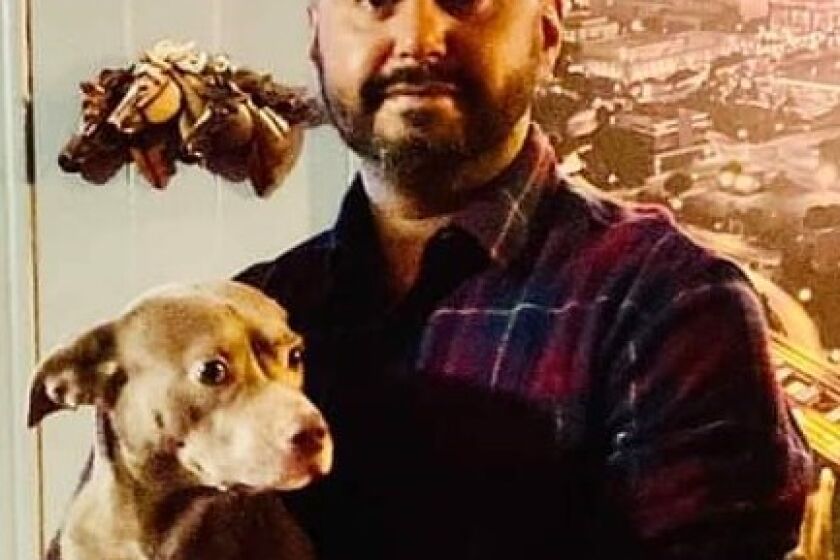 A man with trimmed facial hair poses for a photo while holding a light-brown dog.