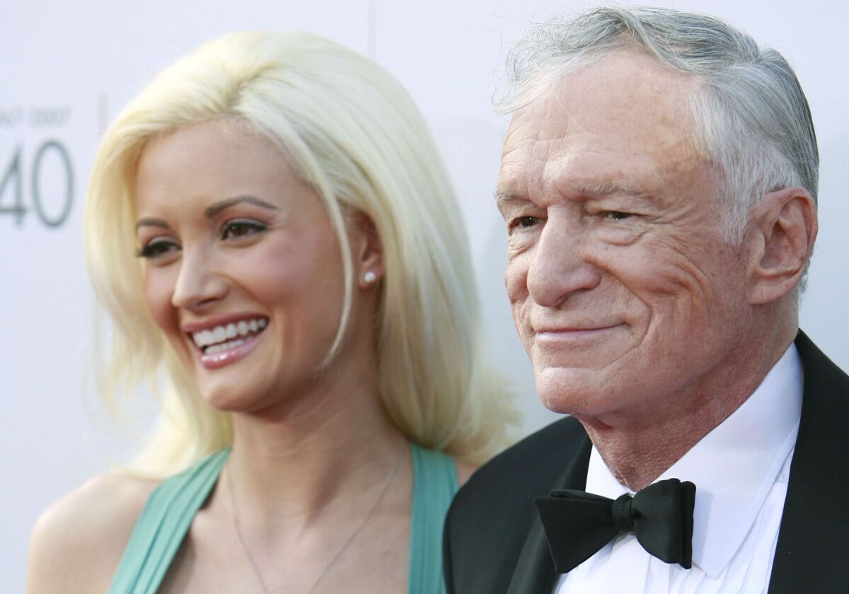 A blonde woman and an older man pose on a red carpet