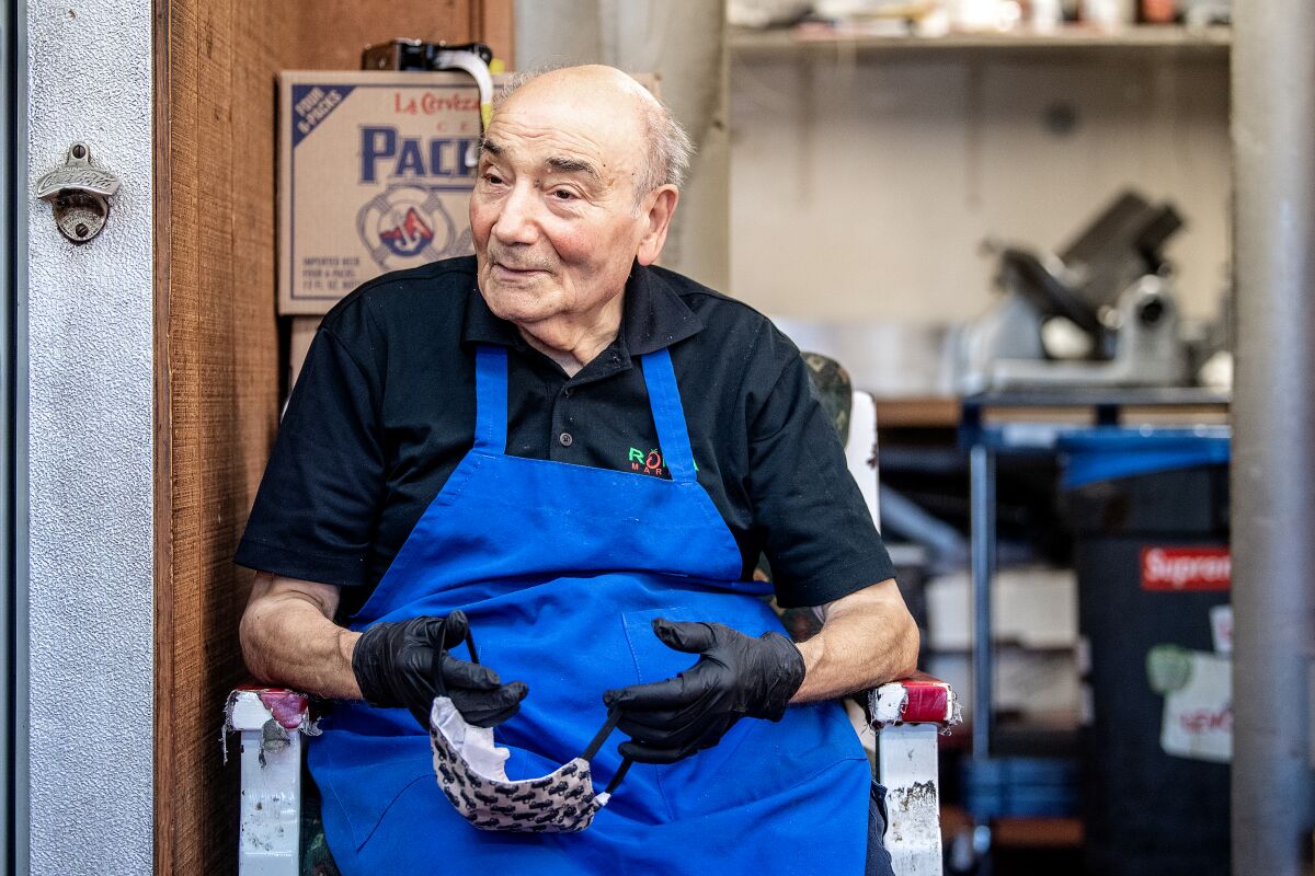 Rosario Mazzeo, owner of Roma Market in Pasadena, puts on a mask and sits in his deli on a recent morning.