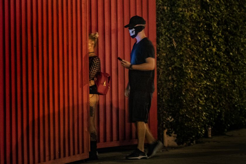 LOS ANGELES, CA - JUNE 12, 2020: Party-goers wearing masks enter through a secret red iron gate to attend an underground rave show during the coronavirus pandemic on June 12, 2020 in Los Angeles, California. Even as COVID-19 cases spike in CA, and the state continues to prohibit concerts and large gatherings, some in L.A.'s underground rave scene have decided it's over, and they're beginning to throw after-hours shows again.(Gina Ferazzi / Los Angeles Times)