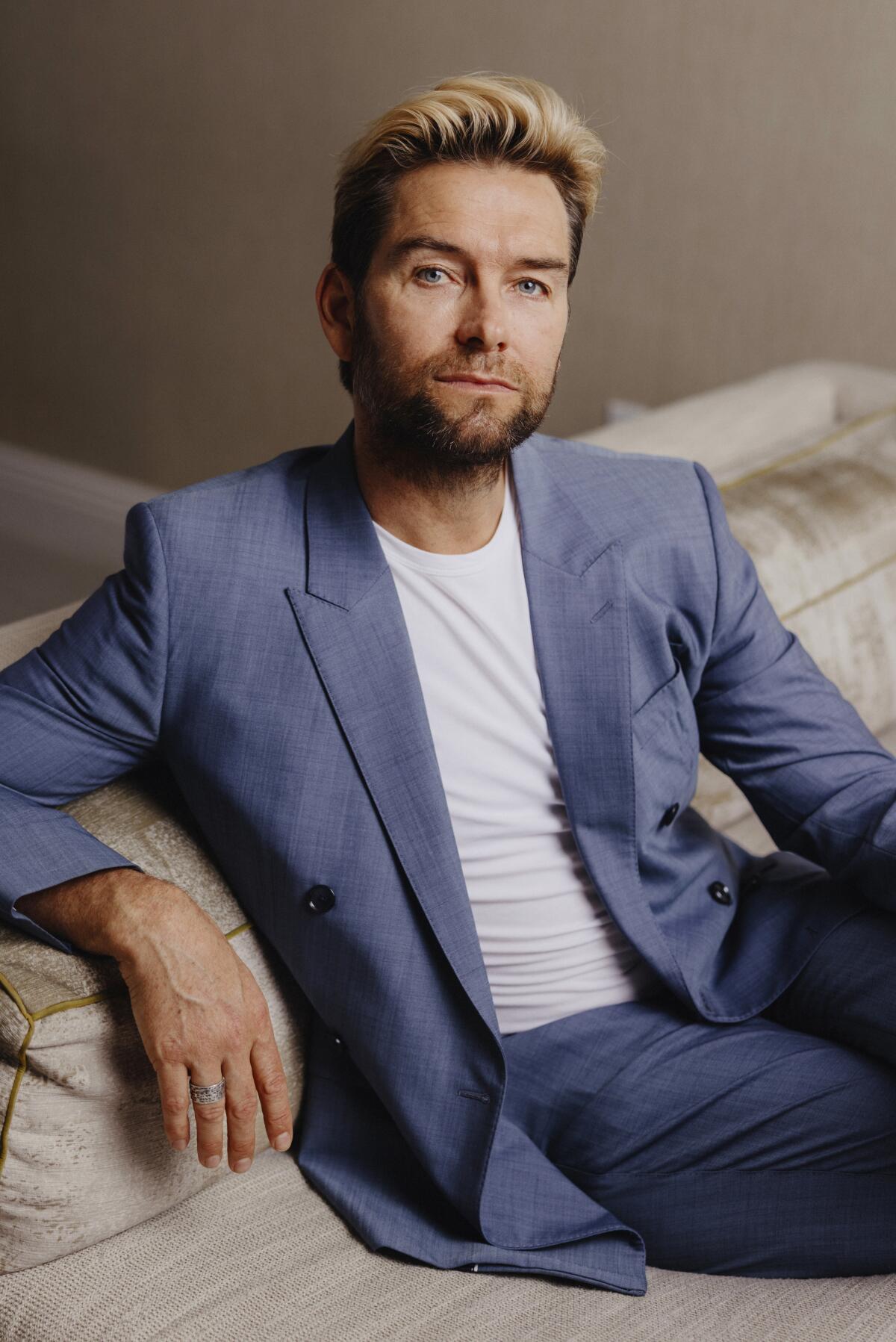 Actor Antony Starr in a suit and T-shirt, sits on a couch for a portrait. 