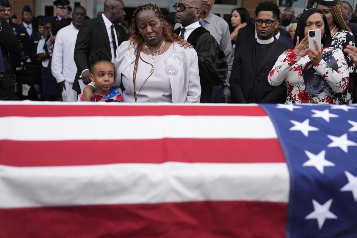 Mourners stand near a flag-draped coffin. 