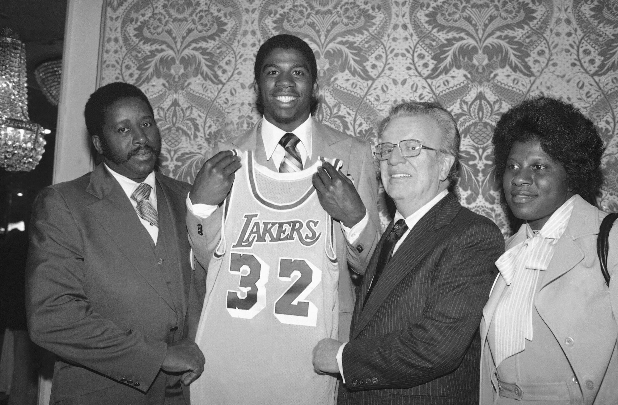 Magic Johnson holds a Los Angeles Lakers uniform, joined by NBA Commissioner Larry O'Brien and his parents. 