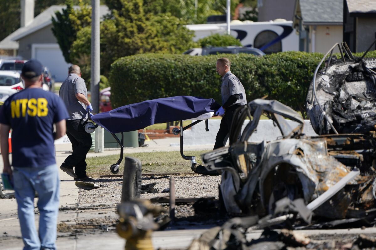 Officials from the San Diego County medical examiners office remove a gurney carrying remains from the site of a plane crash Tuesday, Oct. 12, 2021, in Santee, Calif. Recordings indicate the pilot of a twin-engine plane nose-dived into this San Diego suburb Monday despite a growingly concerned air traffic controller who repeatedly warned the pilot to climb in altitude — information that will be examined by investigators who arrived at the crash scene on Tuesday. (AP Photo/Gregory Bull)