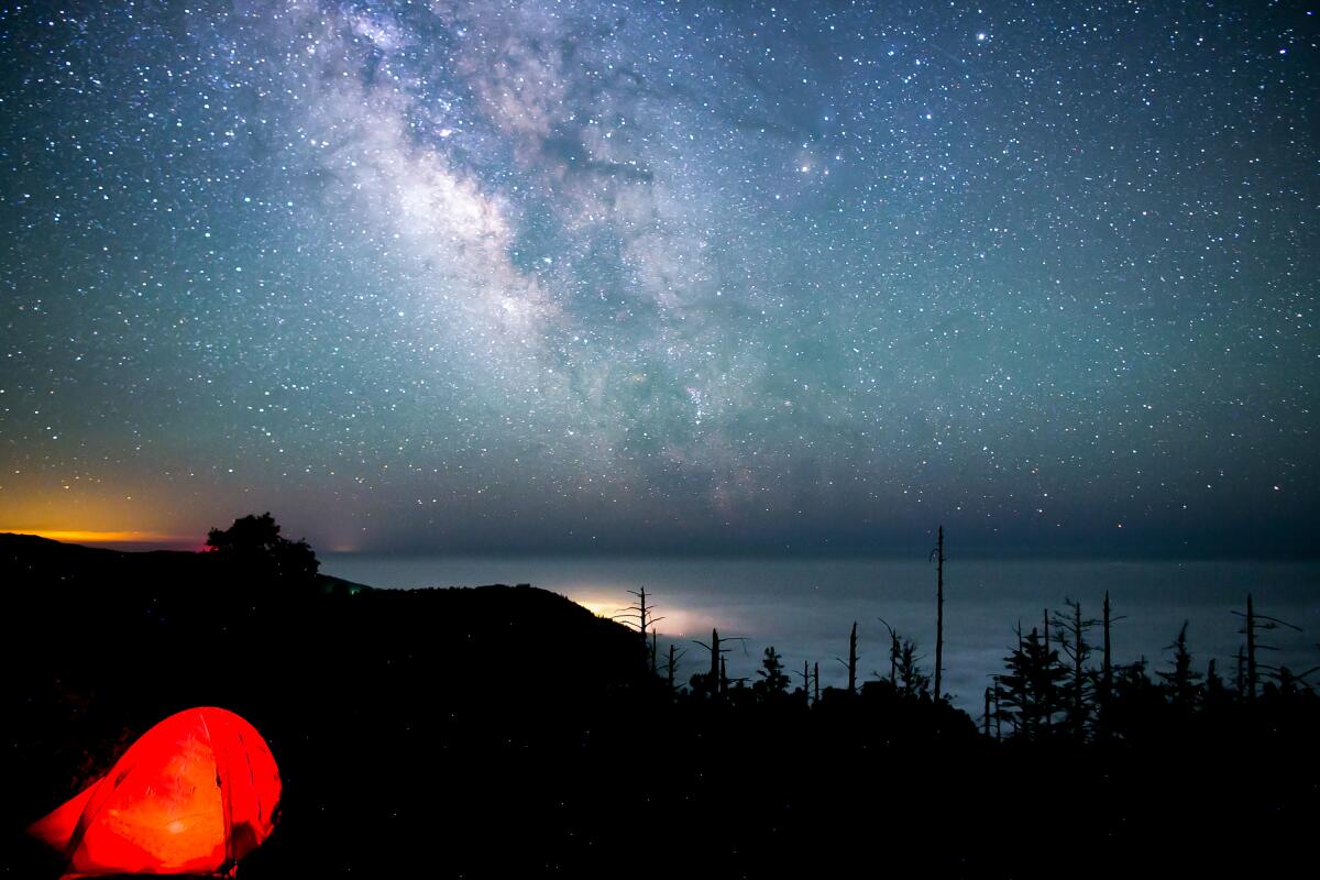 A starry night sky over foggy coastline, seen in the distance.