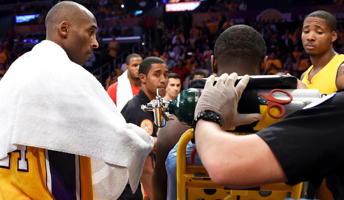 Lakers guard Kobe Bryant, left, comforts teammate Julius Randle as he is wheeled away on a stretcher after breaking his leg in the season opener on Tuesday night at Staples Center.
