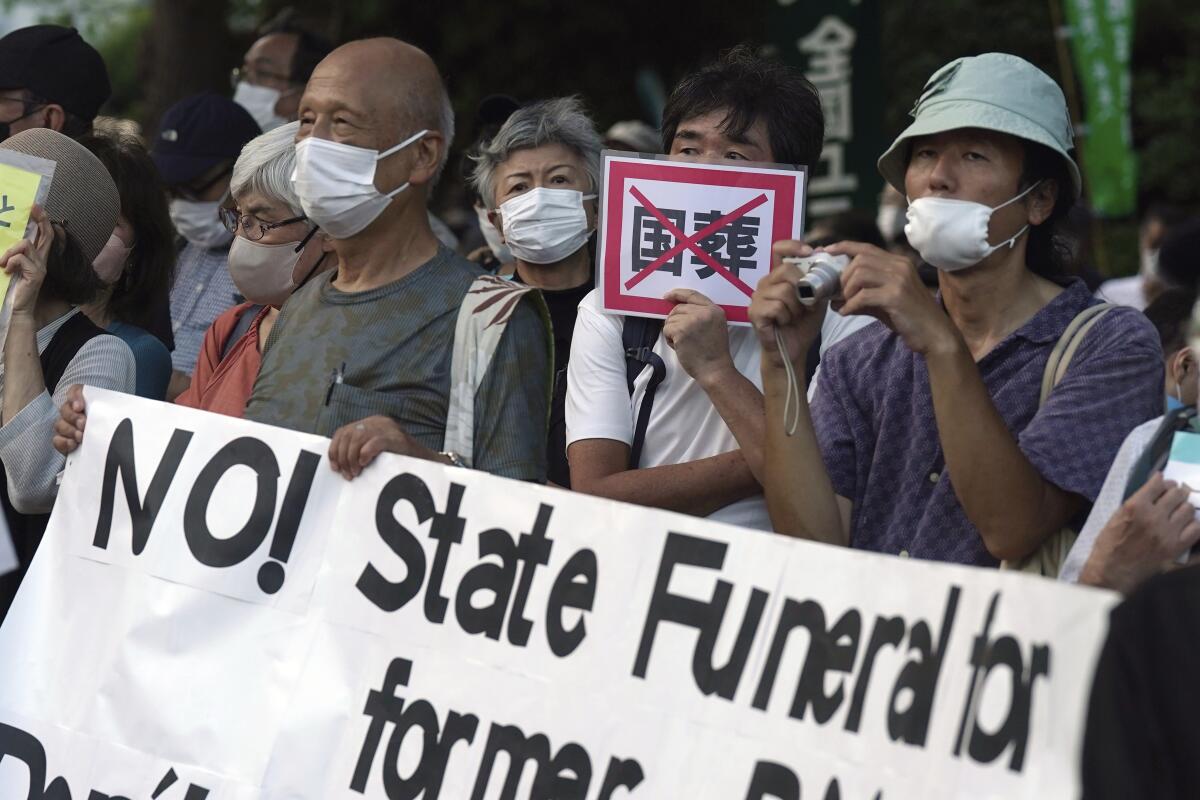 People protest with signs against the state paying for Shinzo Abe's funeral.