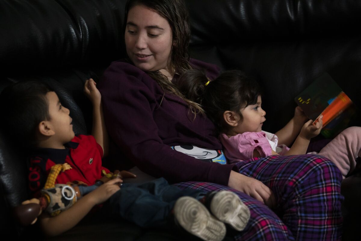 A mother sits on a couch with her two young children