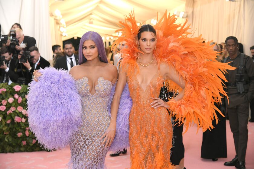 A woman in a feathery purple dress poses with a woman in a feathery orange dress