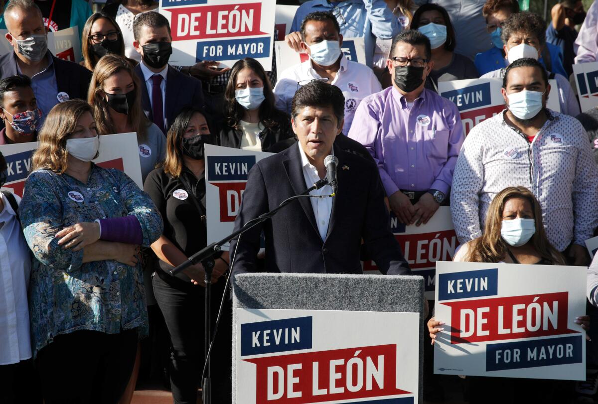 Los Angeles City Councilman Kevin de León speaks at a microphone, backed by masked supporters.