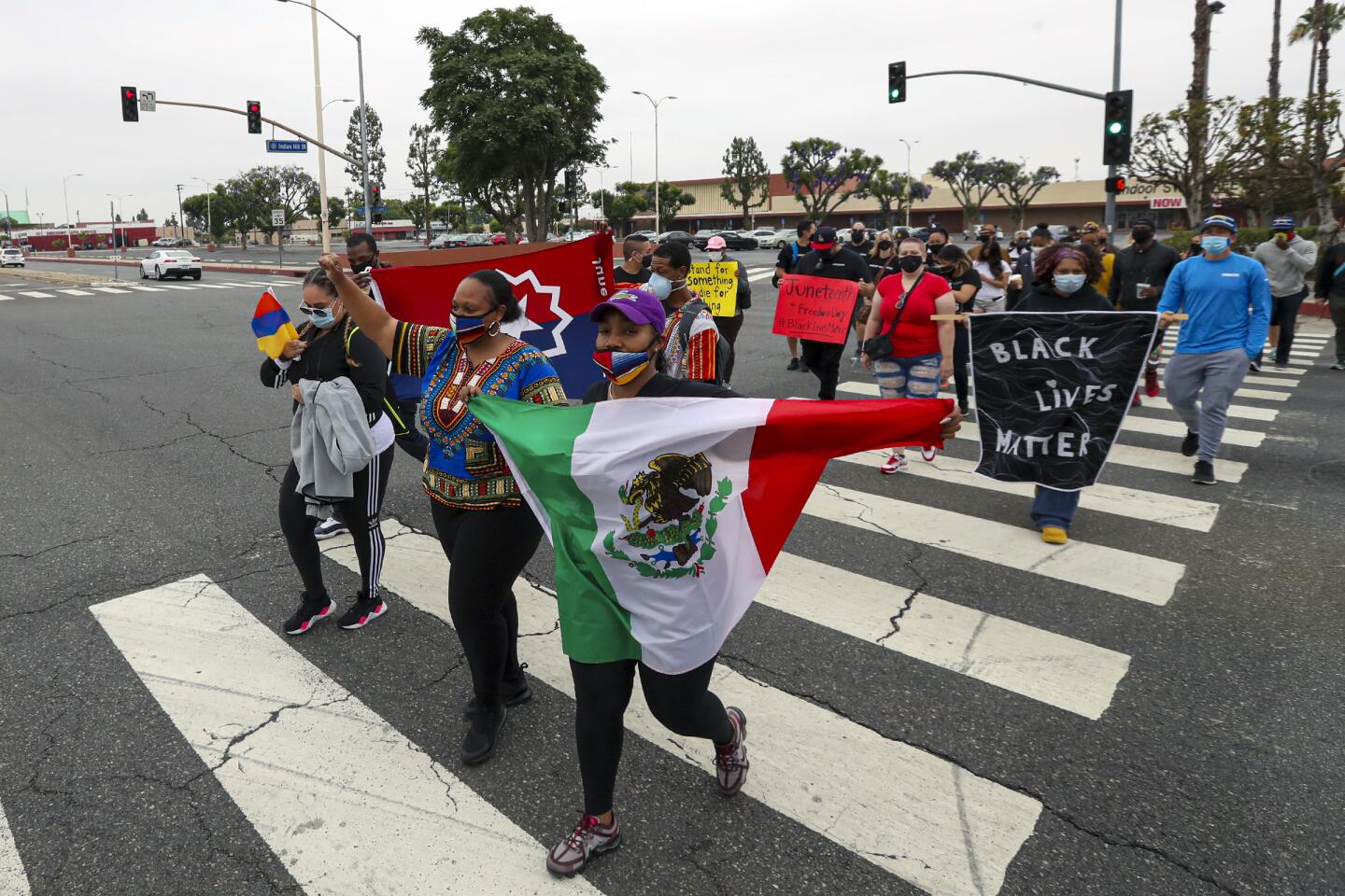 People wave flags and signs while crossing the street during a Juneteenth march in Pomona