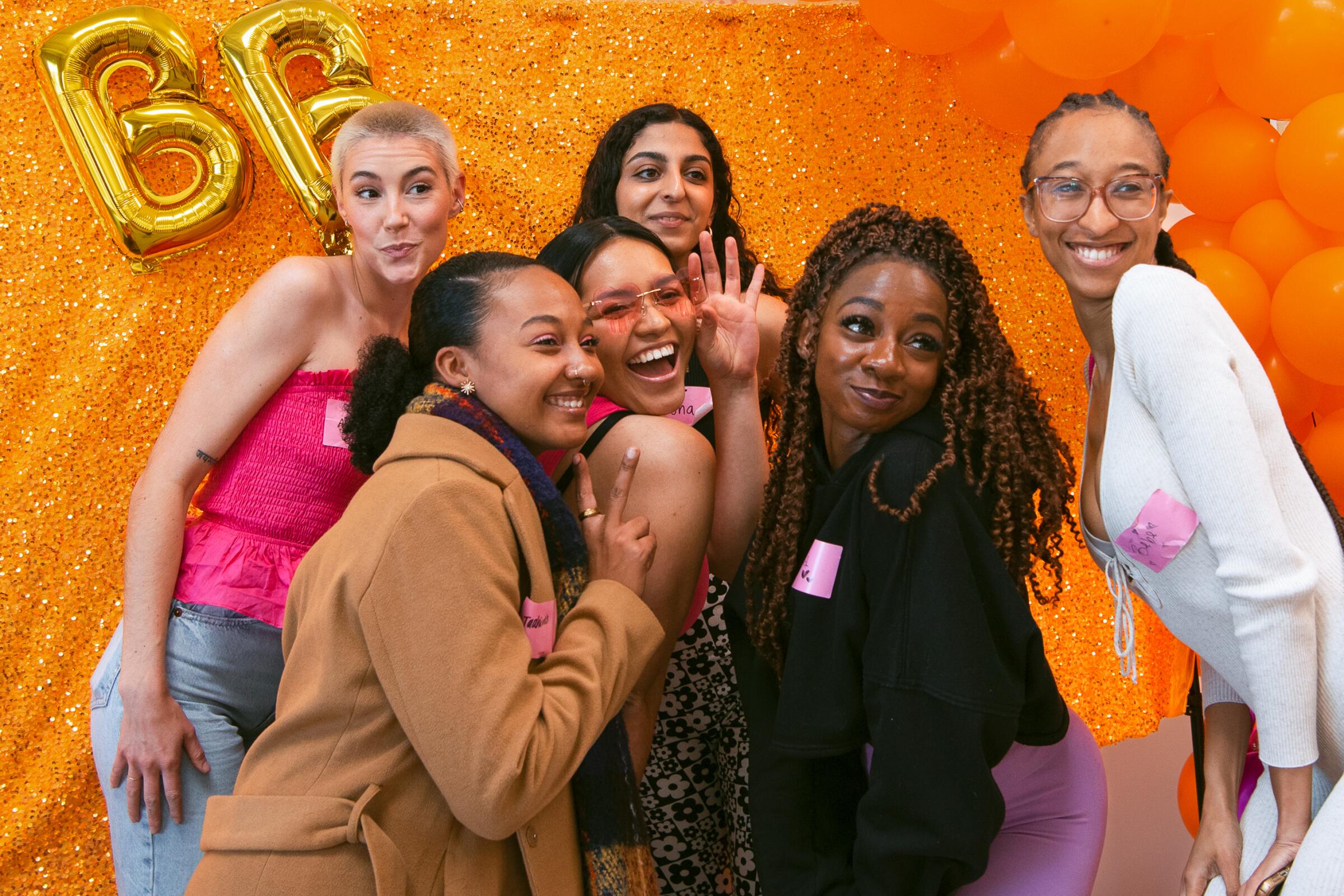 A group photo of women standing against an orange background, smiling