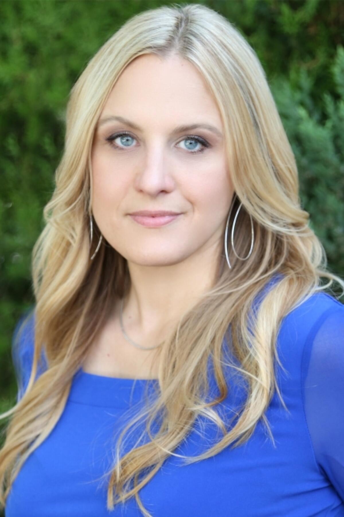 A blond woman in a blue shirt smirks at the camera.