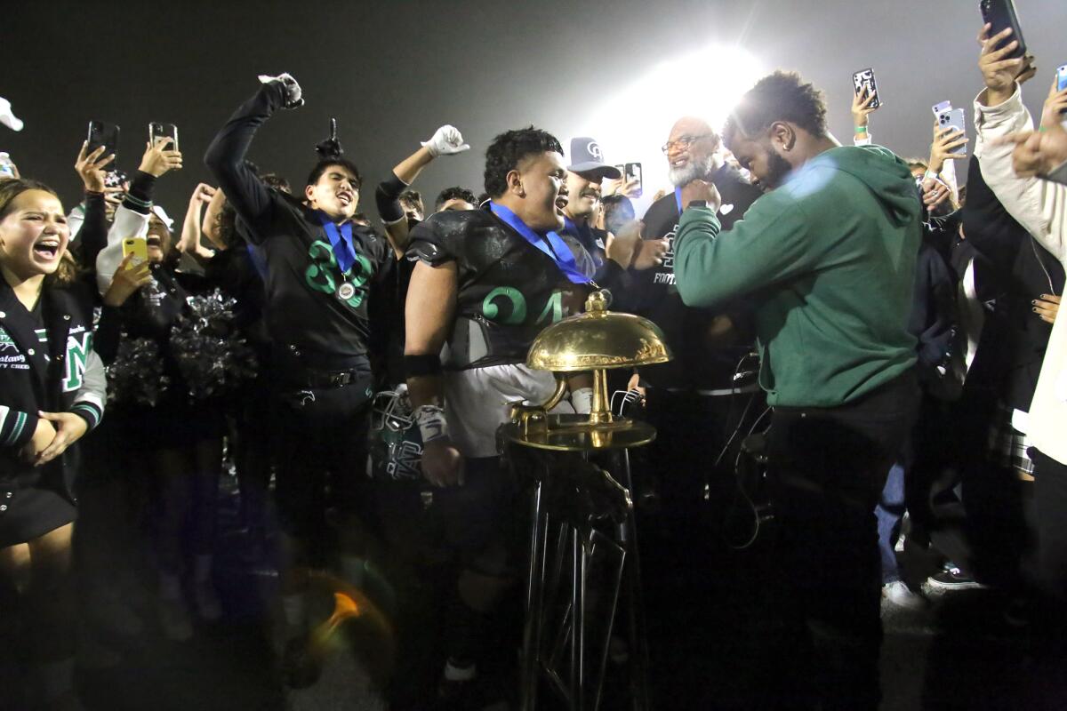 The Costa Mesa High football team celebrates after winning the Battle for the Bell game against Estancia.