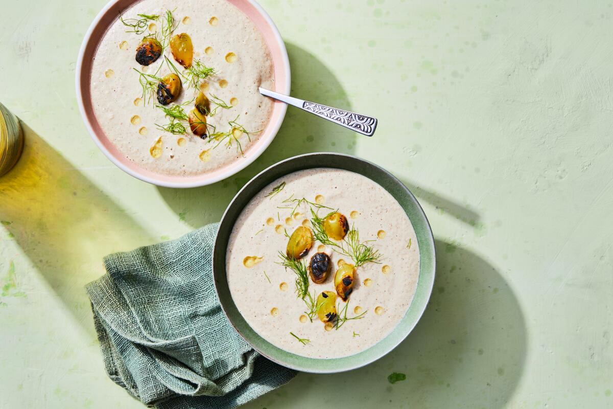Two bowls of creamy soup topped with herbs and grapes