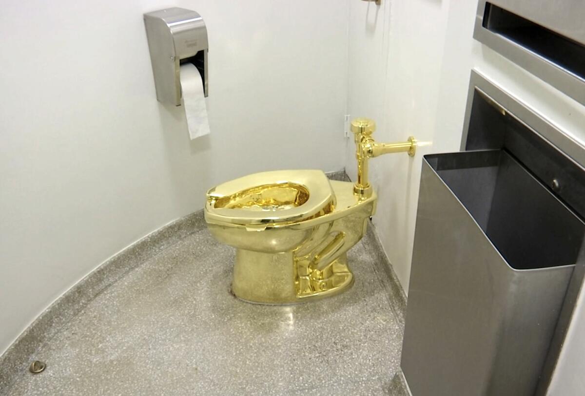 The gold toilet, which was fully functional, sits in a restroom by a roll of paper.