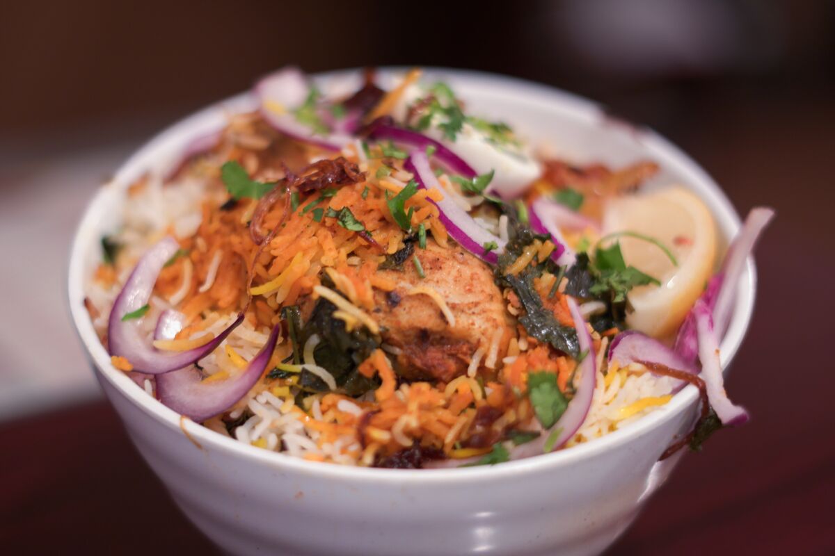 Abhiruchi Grill's chicken dum biryani in a white ceramic bowl, with purple onion, a lemon wedge and herbs