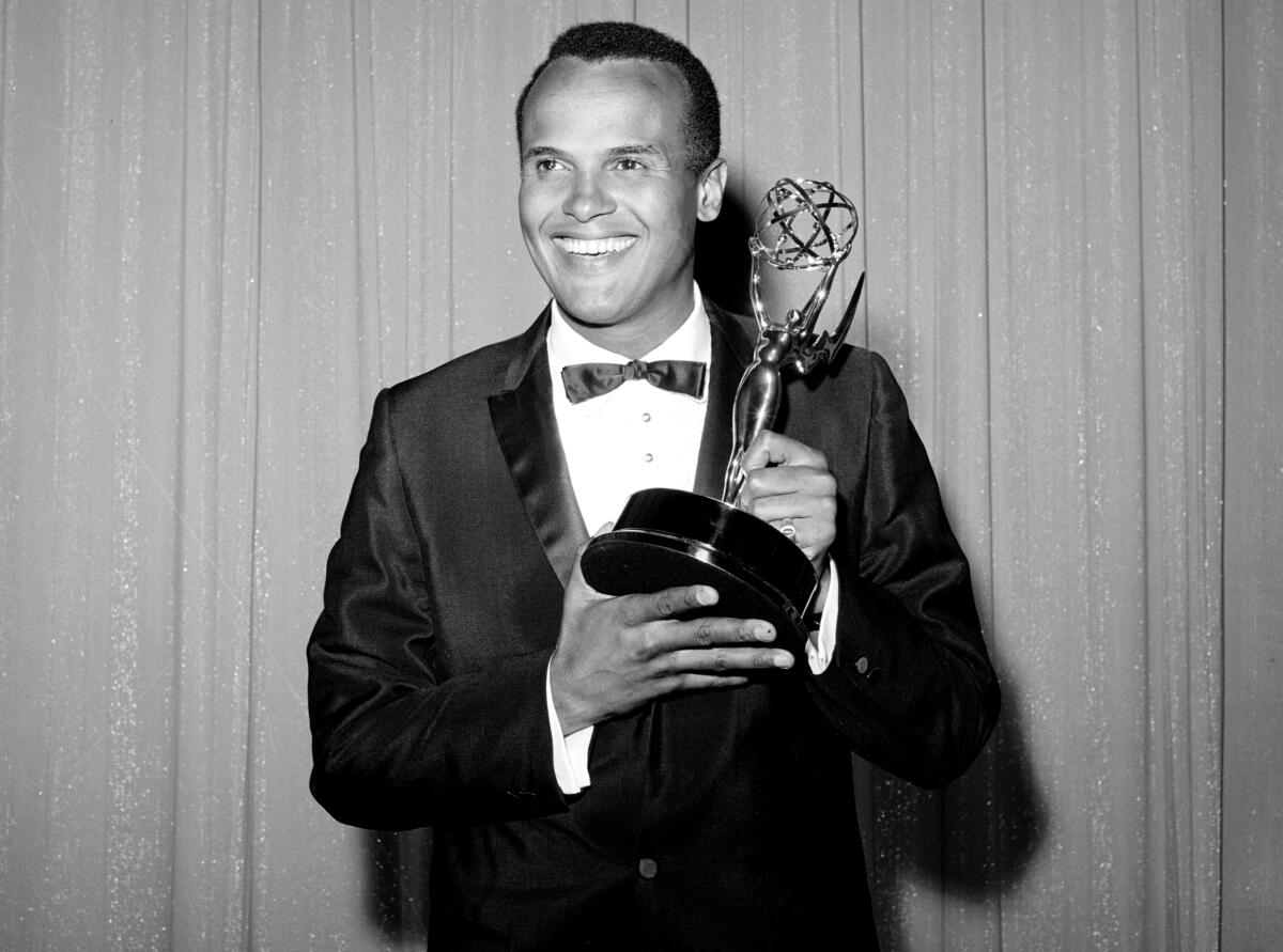 A black-and-white image of Harry Belafonte smiling, wearing a suit and holding an Emmy Award