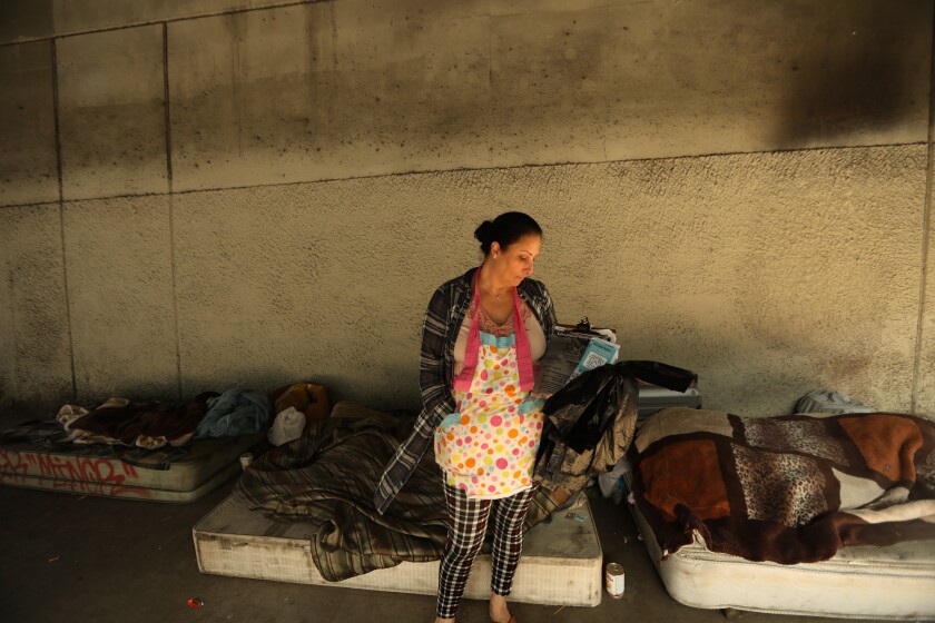 A woman visits a pair of unhoused people under the 60 Freeway.