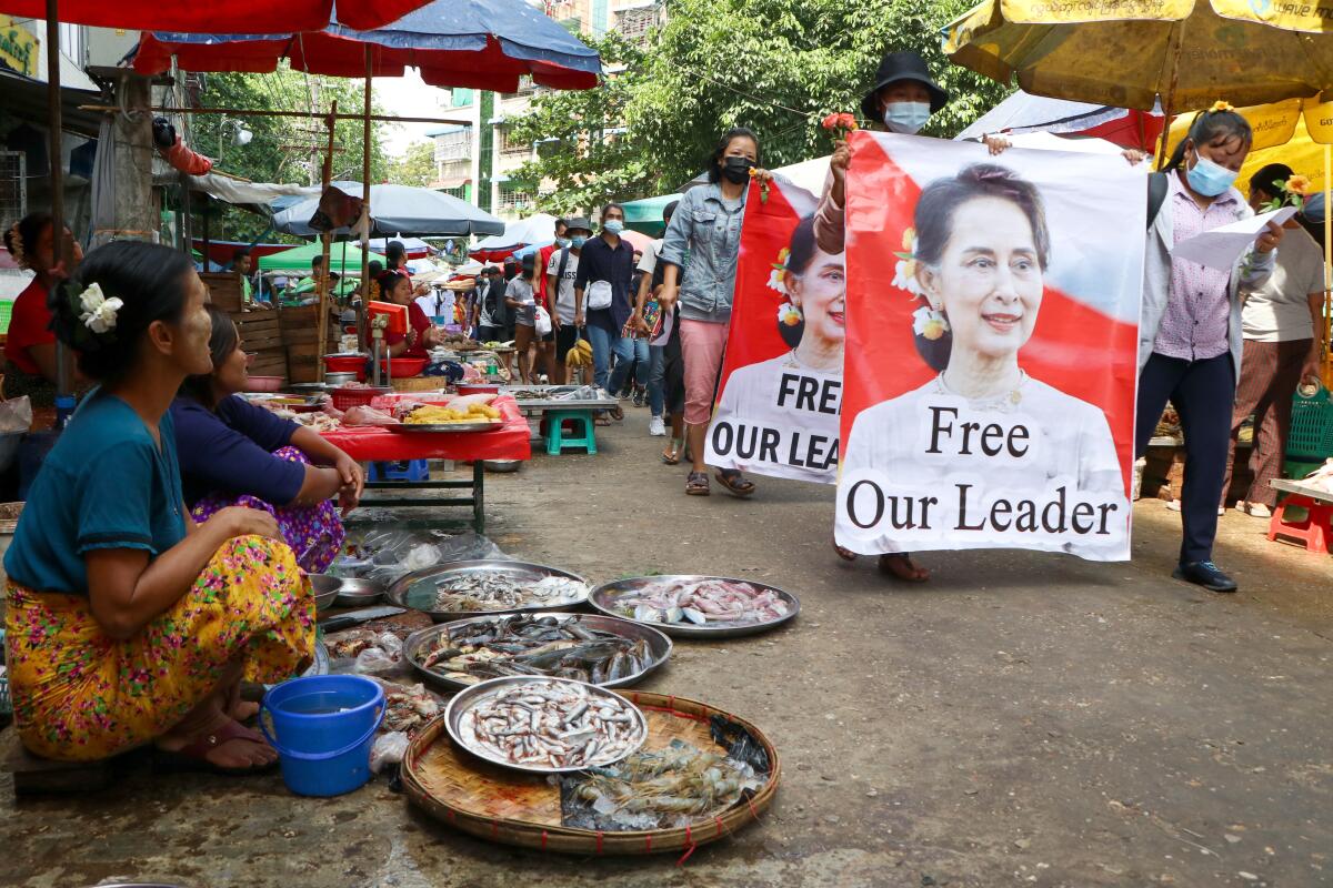 Anti-coup protesters walk through a market with images of ousted Myanmar leader Aung San Suu Kyi