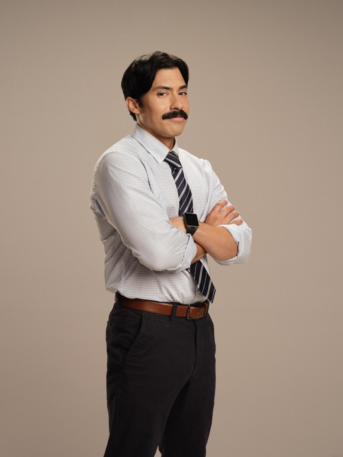 Carlos Santos dressed as his character Ryan, in a shirt, tie and dark slacks with a mustache.