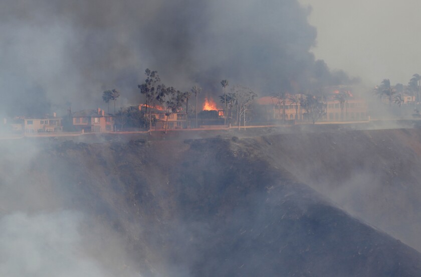 Thick, dark smoke rises from burning homes on top of a ridge