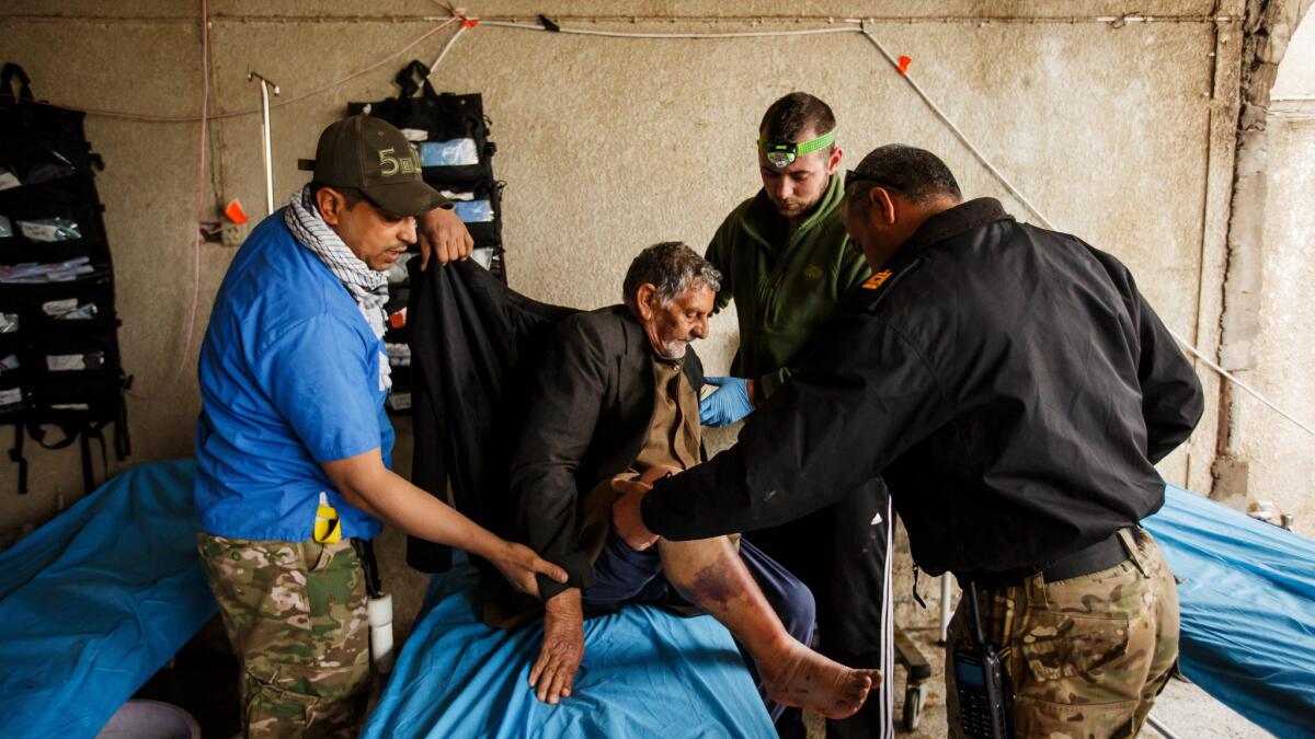 Tom Ordway, 32, second from right, a firefighter from Lake George N.Y., and Maj. Tarek Gazali, right, treat Jadwaa Hamad, 72, at a field clinic near the front lines in Mosul, Iraq. Hamad is suffering from a severely infected burn wound from a recent airstrike.