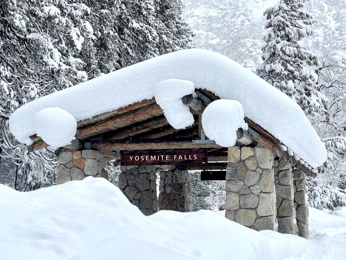 Feet of snow on the ground and covering the roof of a structure with a sign reading "Yosemite Falls"