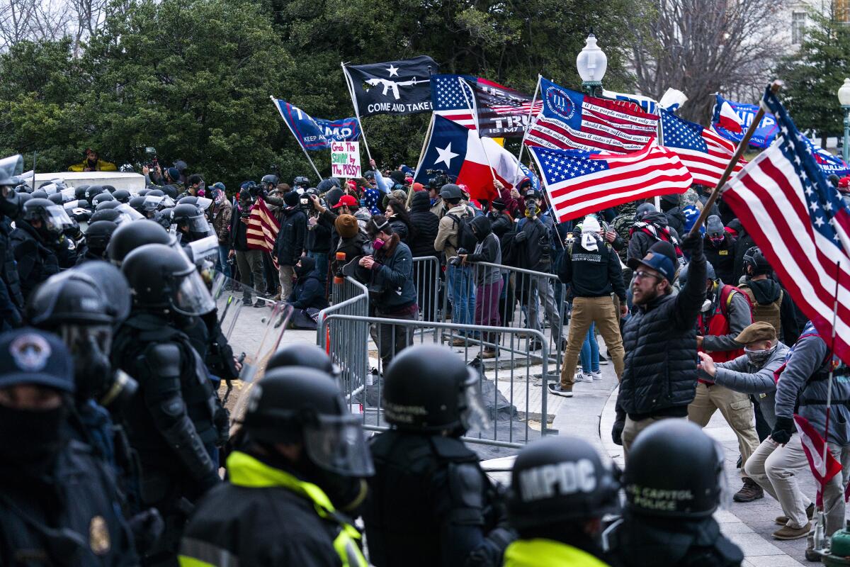 Supporters of then-President Trump bearing flags and storming a line of police and barricades.